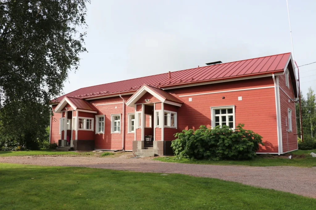 Punaiseksi verhottu puutalo, jossa on valkoiset ikkunalistat ja kaksi sisäänkäyntikatosta.